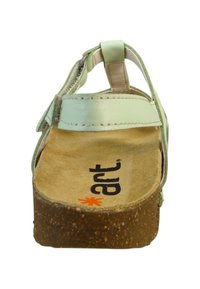Sandalia de cuero verde claro con correa ajustable, suela de tipo corcho y plantilla suave beige que presenta una marca en negro y naranja.