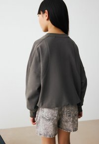 Sweatshirt gris court avec un col rond et des manches raglan, associé à un short en denim texturé gris clair avec des poches arrière.