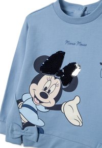 Sweatshirt bleu avec un graphique de Minnie Mouse portant une robe bleue, un nœud noir pailleté et un nœud en tissu près du poignet.
