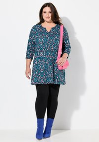 Blauwe en roze gestreepte tuniek, met 3/4 mouwen, gecombineerd met zwarte leggings en blauwe enkellaarzen, accessorized met een roze schoudertas.