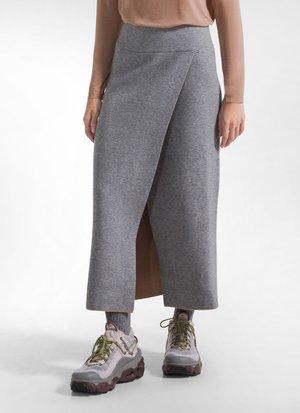 Persoon draagt een grijze wikkel midi-rok, lichtbruine top, grijze sokken en chunky sneakers met groene veters op een witte achtergrond.