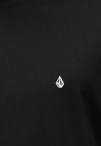 Μαύρο βαμβακερό μπλουζάκι με μικρό λευκό κεντημένο λογότυπο στην αριστερή πλευρά του στήθους; κλασικός λαιμός τύπου crew και λεία υφή.