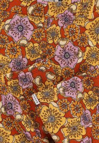 Stof met bloemmotief met levendige oranje, paarse en gele bloemen met een textuur uiterlijk. Etiket zegt "LOOKS."