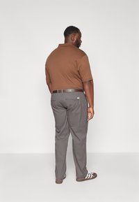 Bruine polo en een grijze broek met een bruine riem. De outfit heeft korte mouwen, rechte pasvorm broeken en casual schoenen.