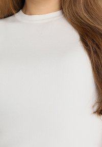 Bílý pruhovaný top s krátkým rukávem a kulatým výstřihem, s hladkou texturou a přiléhavým střihem.