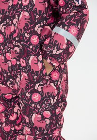 Pink mønsteret vinterdragt med blomster- og dyremotiver på en mørk baggrund, med en reflekterende bånd på ærmet og lommeåbninger.