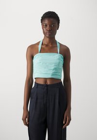Un crop top aqua avec texture froncée et des liens à fines bretelles. Associé à un pantalon large bleu marine, créant un look contrasté.