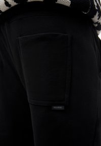 Black pants close-up showing a rectangular side pocket with a small "PULL&BEAR" label beneath the pocket flap.