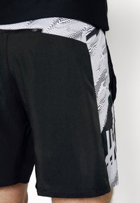 Pantalones cortos negros con una textura suave, panel lateral con un patrón en blanco y un pequeño logo, diseñados para la comodidad y el uso activo.