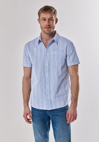 Korte mouwen overhemd met knopen in het wit met blauwe verticale strepen. Voorzien van een borstzak en een klassieke kraag. Draagt met blauwe jeans.