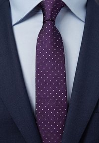 Lila slips med vita prickar, gjord av texturerad tyg, bärs över en ljusblå skjorta, kombinerad med en mörkblå kavaj.