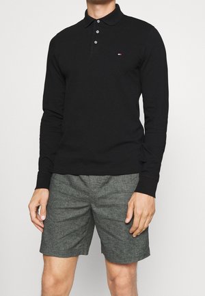 Czarna koszulka polo z długim rękawem, zapięcie na trzy guziki, materiał bawełniany, dopasowany fason oraz mały detal logo na klatce piersiowej; zestawiona z szarymi szortami.