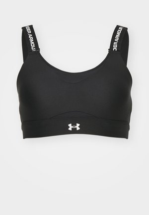 Soutien-gorge de sport noir avec une texture douce et un col rond. Il possède des bretelles larges avec le logo "Under Armour" et une marque sur le devant.