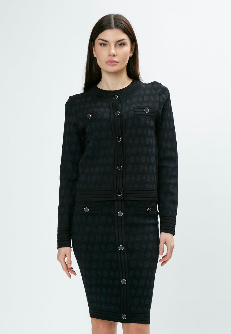 Schwarzes Zweiteiler-Outfit bestehend aus einer strukturierten, knöpfbaren Jacke und einem Rock, mit kontrastierenden Mustern, runden Knöpfen und taillierter Passform.