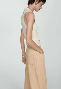 Lichtbeige ribbelige mouwloze top met een kraag, gecombineerd met losse beige broeken met zijzakken en een zachte textuur.