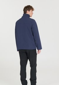 Marinblå vattentät jacka med hög krage, sömlösa axlar och rak passform. Buren över svarta byxor, har en minimalistisk design utan synliga logotyper.