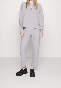 Grey sweatshirt with a half-zip collar and ribbed cuffs, paired with matching grey tapered sweatpants. Black chunky loafers complete the look.