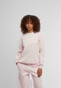 Világos rózsaszín pulóver, puha anyagból készült, hosszú ujjakkal és kerek nyakkivágással. Finom hímzett részletek a mellrészen.