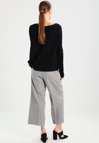 Musta neulepaita, jossa on löysä istuvuus ja leveä kaula-aukko, yhdistetty harmaisiin leveälahkeisiin housuihin. Asun viimeistelevät mustat korolliset mules-kengät.