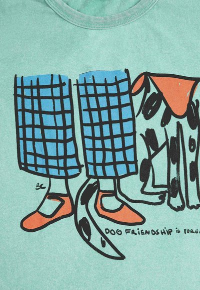 Donji dijelovi nogu u plavim kariranim hlačama i narančastim cipelama pored crno-bijelog psa s narančastom mrljom na glavi.