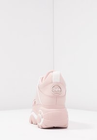Rosa sneakers med vita detaljer, slätt syntetmaterial, rundad form och kraftig sula. Har en logotyp på hälen och en dragflik.
