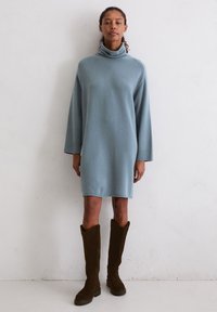 Jasnoniebieska, oversize sukienka z golfem i długimi rękawami. Miękka tekstura. Zestawiona z wysokimi, ciemnobrązowymi zamszowymi botkami. Gładkie wykończenie.