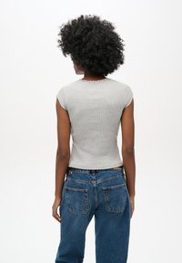 Top gris de manga corta con canalé y escote con forma de ondas, combinado con unos vaqueros azul de tiro alto que tienen bolsillos traseros y un cinturón.