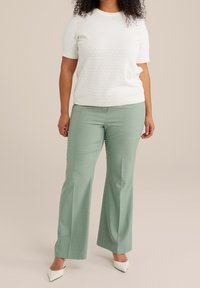 Biały, teksturowany top z krótkim rękawem i okrągłym dekoltem, zestawiony z jasnozielonymi, dopasowanymi spodniami i białymi, spiczastymi szpilkami, stojący na neutralnym tle.