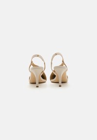 Nude high-heeled sandals with an open back, slim ankle strap, and a smooth leather texture. They feature a subtle gold accent on the strap.
