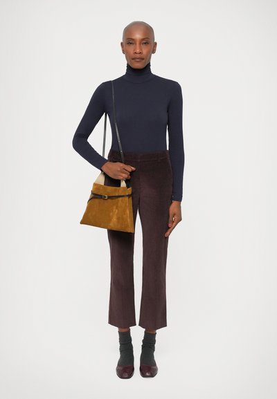 Brune kordfløjspants, navy turtleneck, tekstureret gul taske med sorte accenter, grå sokker og maroon sko. Enkel, struktureret design.