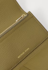 Zielona oliwkowa skórzana portmonetka o teksturowanym wykończeniu, ze złotą zamkiem błyskawicznym i wytłoczonym logo "MICHAEL KORS". Kompaktowy i usystematyzowany design.