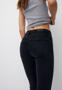 Jean noir skinny avec une texture lisse, présentant deux poches arrière et une taille haute. Le tissu semble extensible et ajusté.