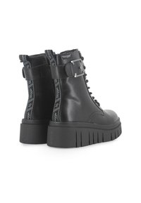 Botas negras hasta el tobillo con suela de plataforma gruesa, material de cuero suave, parte frontal con cordones y acento de hebilla en el lateral. Marca visible en las correas.
