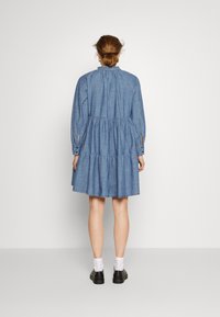 Vestido de ganga azul claro com cintura franzida, mangas compridas e saia em camadas. Apresenta punhos com botões e decote redondo.