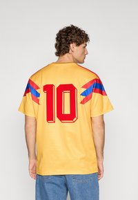 T-shirt gialla a maniche corte con numero rosso "10" e strisce blu-rosse sulle spalle; realizzata in tessuto morbido con vestibilità comoda.