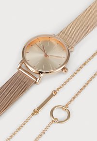 Guld mesh ur med en rund, lys guld ansigt, minimalistiske time markører og et matchende halskæde med en cirkulær kæde og stang vedhæng.