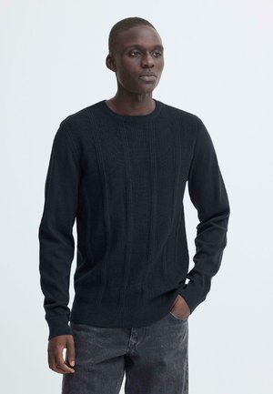 Maglione nero a maglia con trama a coste e scollo tondo. Maniche lunghe, polsini e orlo aderenti. Abbinato a jeans scuri.