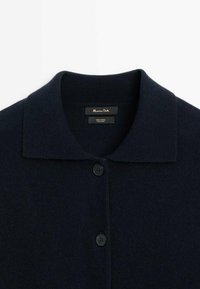 Granatowy kardigan z wełny z płaskim kołnierzykiem, czterema guzikami i gładką teksturą. Metka wskazuje na 100% skład wełny.