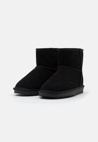 Stivaletti neri in suede con punta tonda, design semplice e suola in gomma testurizzata, caratterizzati da dettagli cuciti lungo le cuciture.