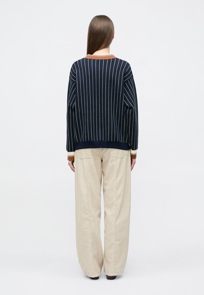 Πλεκτό πουλόβερ με ναυτικό ριγέ, με καφέ γιακά, συνδυασμένο με άνετο μπεζ παντελόνι, και τα δύο με απαλή υφή και casual σιλουέτα.