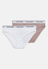 Δύο βαμβακερά εσώρουχα Calvin Klein σε λευκό και μπεζ χρώμα με ελαστικές ζώνες μέσης με λογότυπο, τοποθετημένα επίπεδα σε λευκό φόντο.