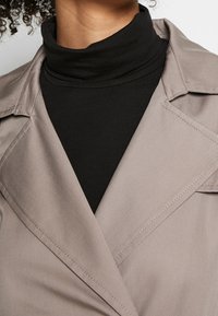 Blazer grigio con tessuto testurizzato, caratterizzato da un colletto a risvolto, indossato sopra un dolcevita nero aderente. Mostra dettagli di cucitura.