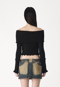 Pull noir à épaules dénudées en maille côtelée avec manches longues, associé à une mini-jupe en jean dotée de poches beiges et d'une chaîne décorative.