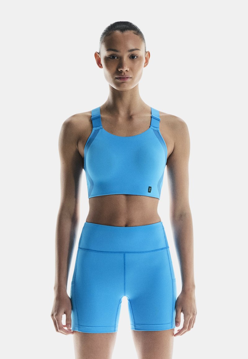 Niebieski sportowy stanik z szerokimi ramiączkami i gładką fakturą, w połączeniu z niebieskimi szortami typu high-waist o dopasowanym kroju i szwach.