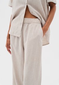 Helles beiges Leinenhemd mit entspannter Passform und Knopfschluss, kombiniert mit passenden Jogginghose im Stil mit elastischem Bund und Taschen.