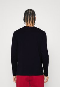 Pitkähihaine tummansininen paita, jossa on pyöreä pääntie, valmistettu sileästä kankaasta. Takana pääntien kohdalla on pieni punainen, valkoinen ja sininen yksityiskohta.