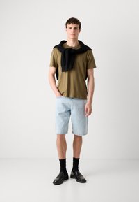 Olivengrønn t-skjorte, lyseblå denimshorts, svart genser knyttet rundt skuldrene, svarte sokker, og svarte loafers. Enkel, uformell antrekk.