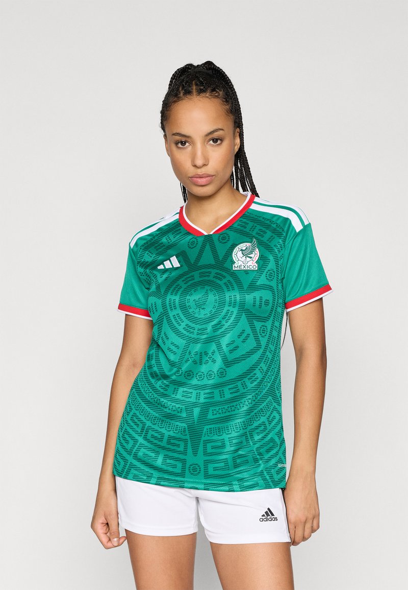 Camisa de futebol da seleção mexicana verde, com um padrão circular, detalhes em branco e vermelho, e o logótipo da Adidas no lado esquerdo do peito.