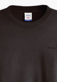 Sudadera negra de manga larga y cuello redondo, confeccionada en un material suave, con un cuello acanalado y un logo bordado en el pecho.
