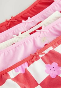 Drei Paare Unterwäsche mit elastischen Taillenbändern: rot uni, pink mit Blumenmuster und weiß mit rot kariertem Design. Jedes hat Schleifendetails.